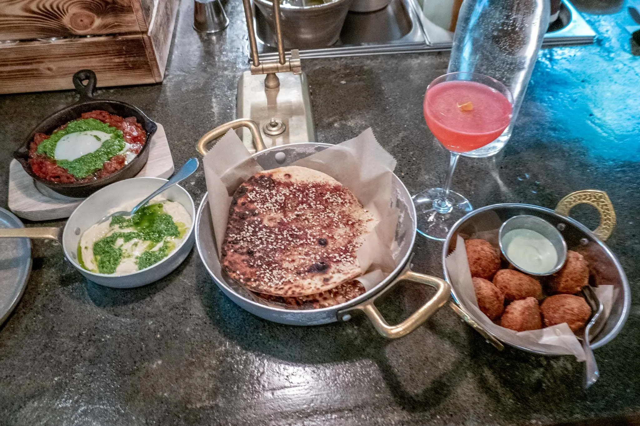 Pita, hummus, a cocktail, and other dishes on a counter.