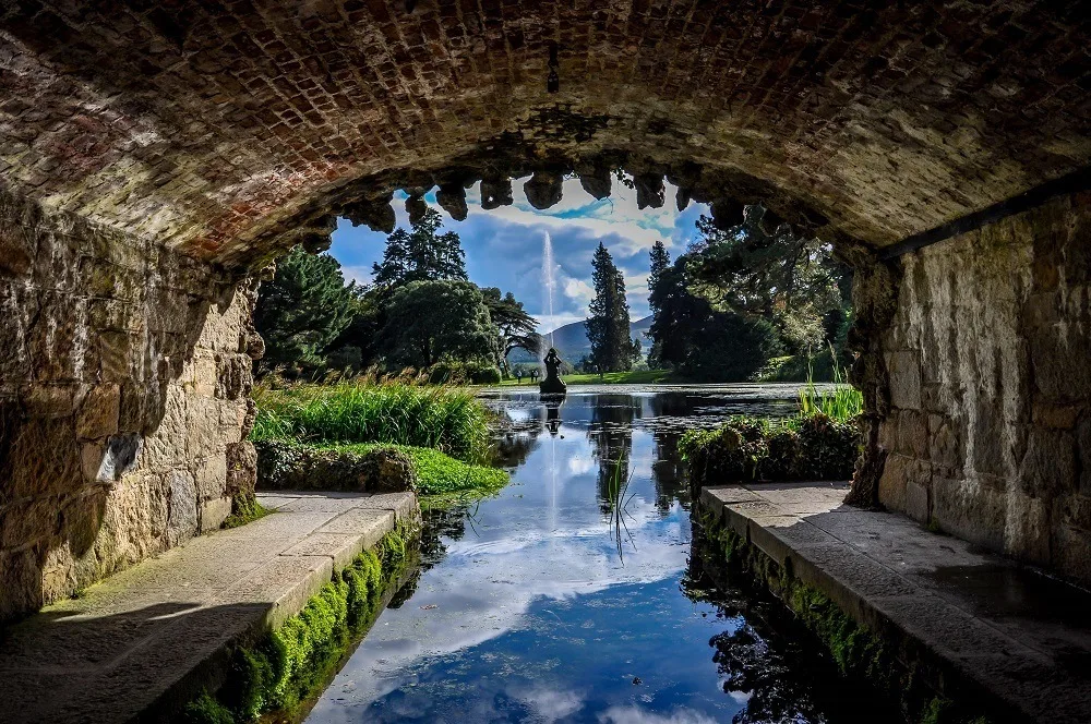 Fountain in a pond viewed through the arch of a bridge