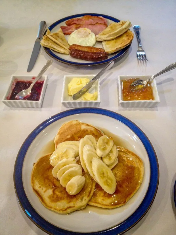 Pancakes topped with bananas, sausage, eggs, and other breakfasts foods on a table