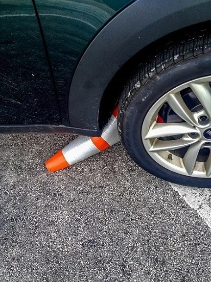 Orange traffic cone stuck under car wheel