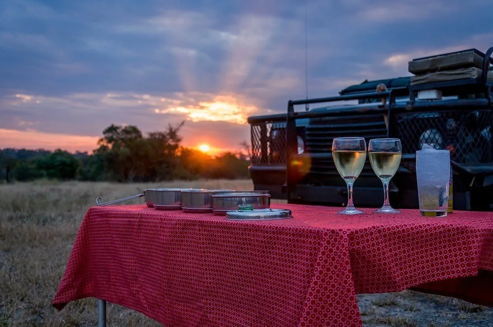 Wine glasses on red tablecloth in front of the safari Land Rover at sunset
