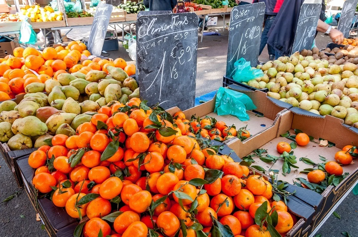 Oranges and pears for sale in crates on a table alongside signs advertising them in French