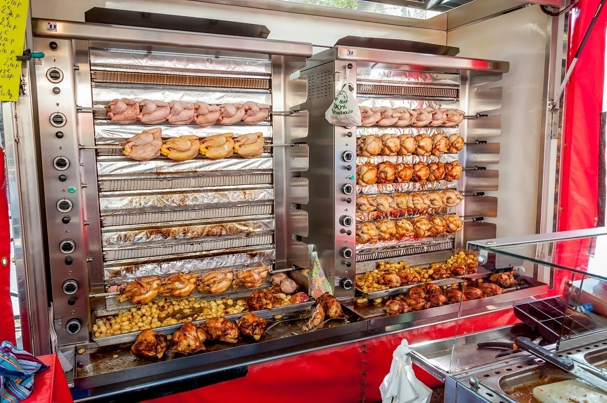 Rotisserie chickens cooking at an outdoor market