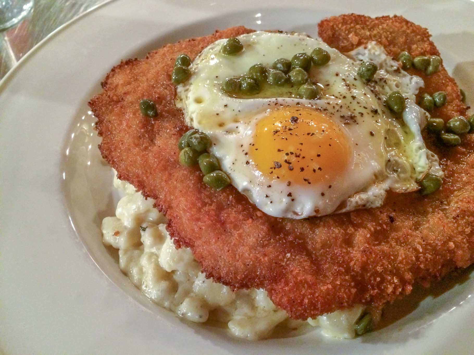 Schnitzel topped with a fried egg and capers on a plate.