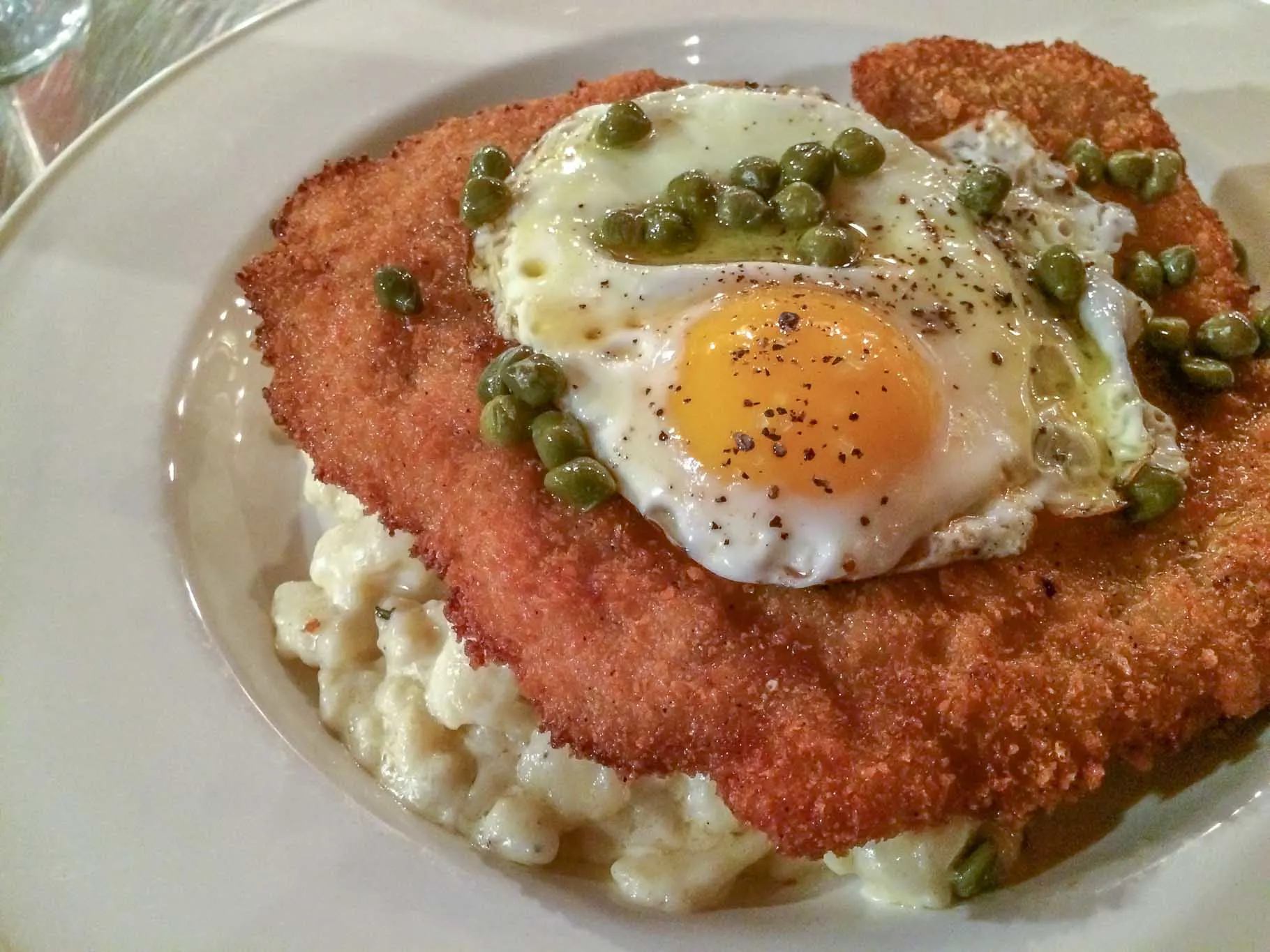 Close up of schnitzel topped with fried egg and capers on a plate.