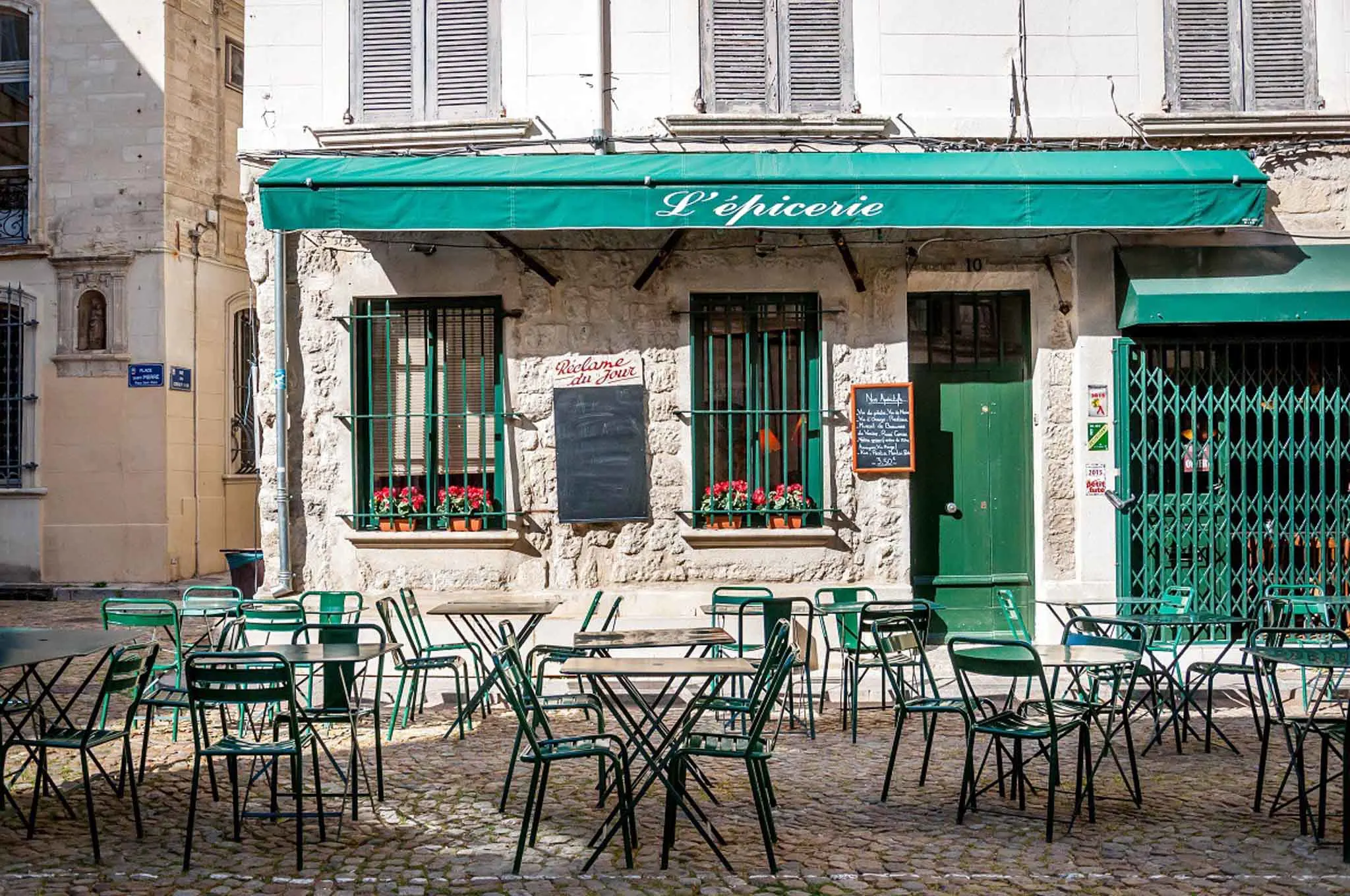 Tables and chairs in front of a cafe with a green awning.