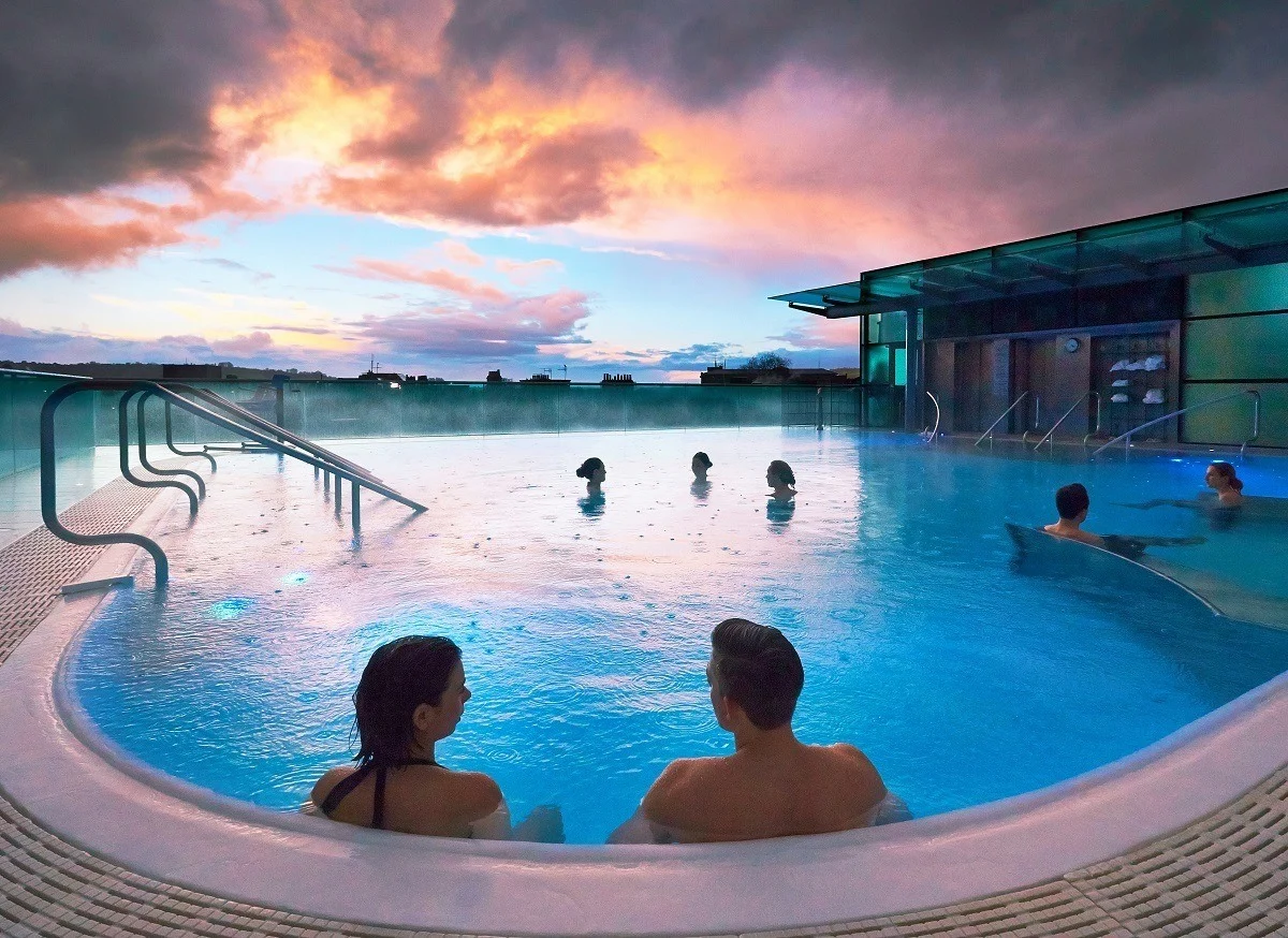The open-air rooftop pool at the Thermae Bath Spa at sunset