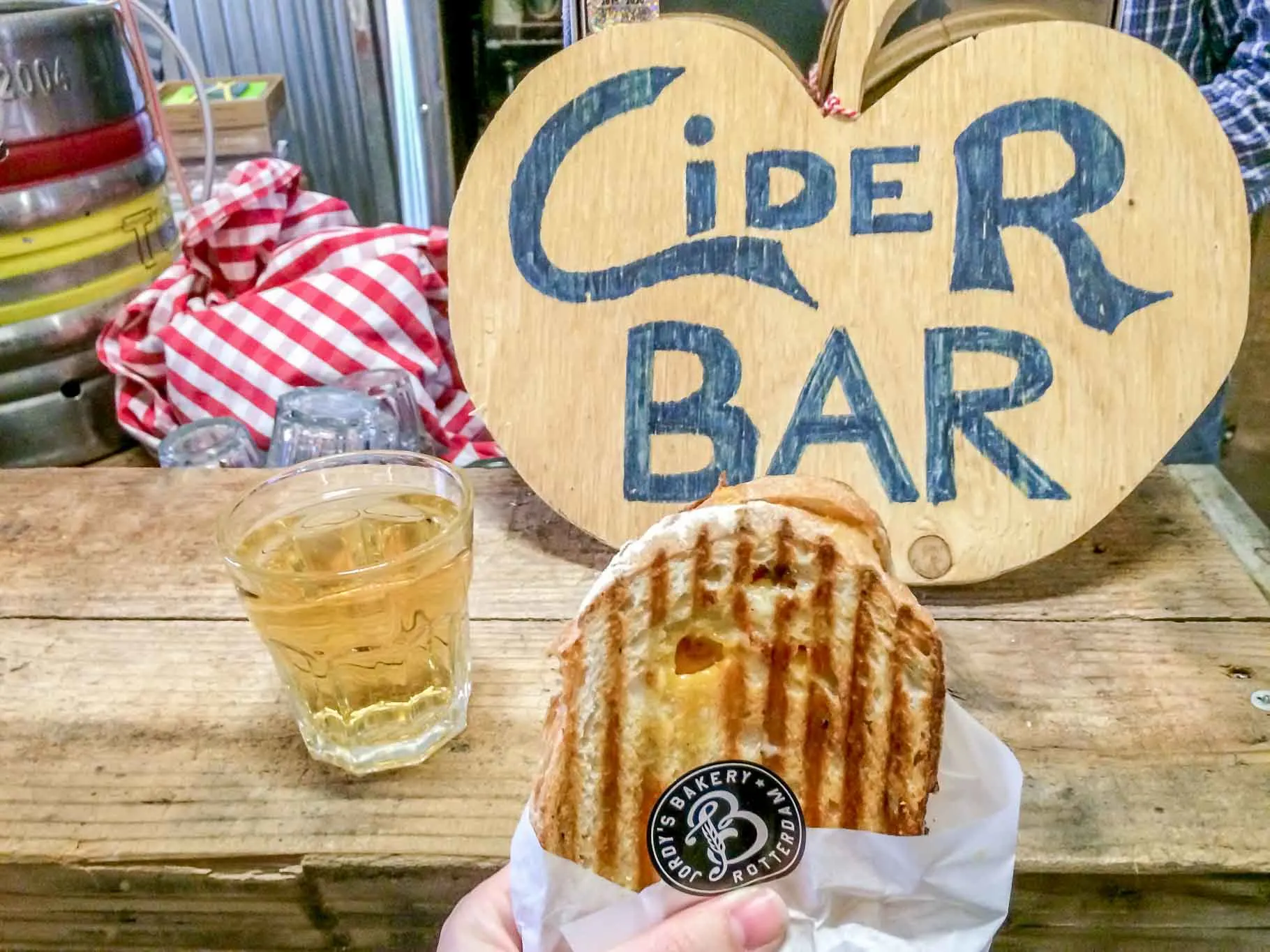 "Cider Bar" sign, sandwich, and drink on a table