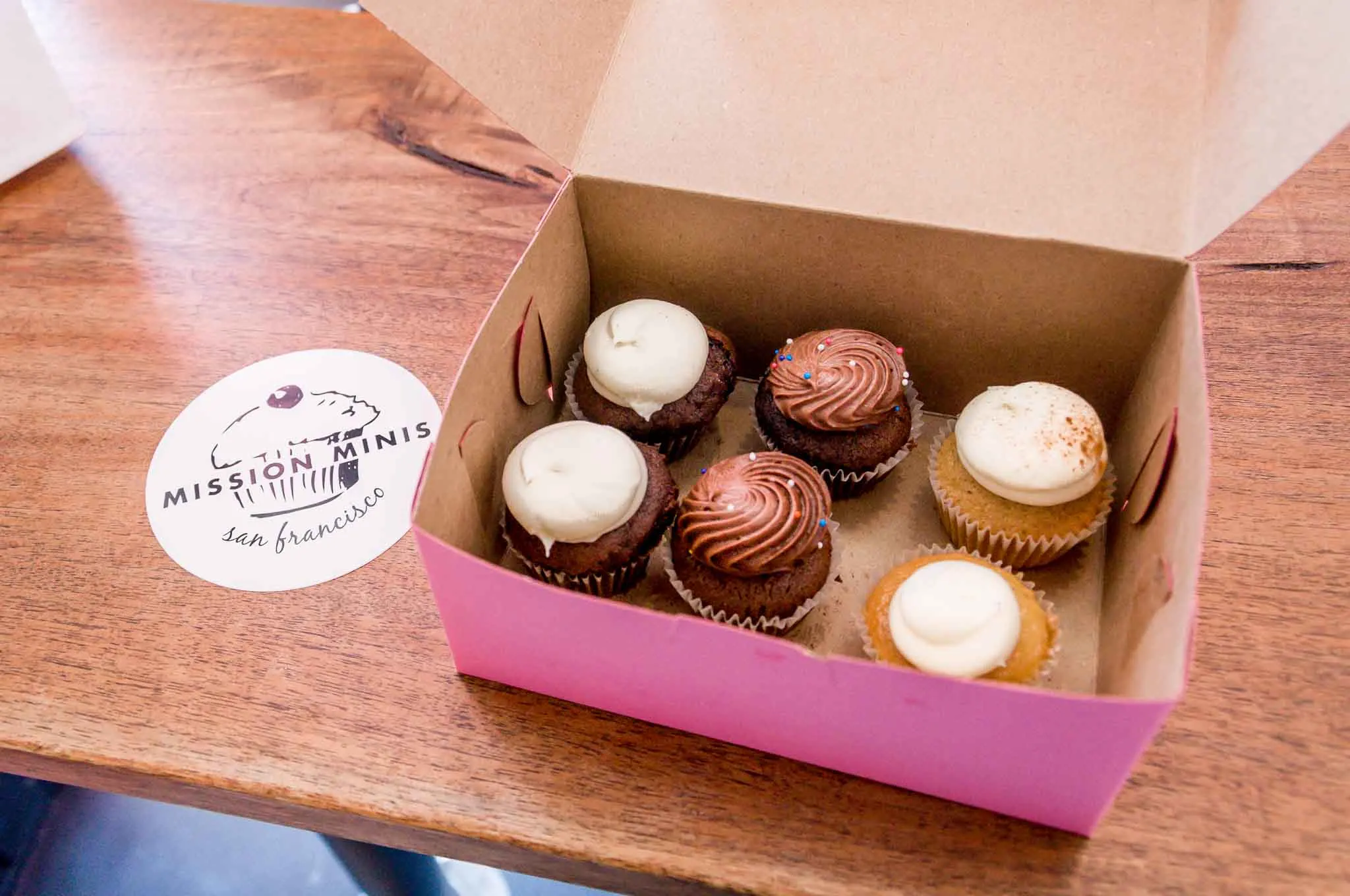 Box of mini cupcakes beside a "Mission Minis" coaster. 
