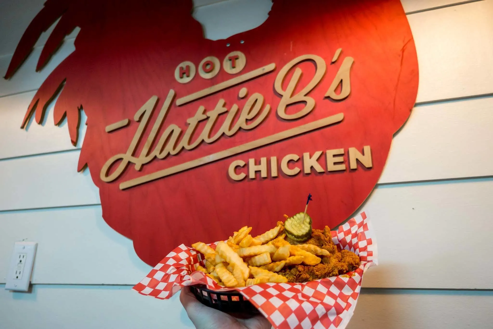 Basket of hot chicken in front of a Hattie B's sign.
