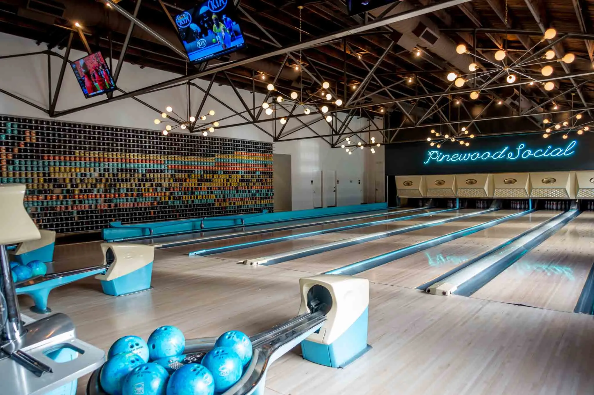 Bowling lanes with turquoise accents and a turquoise neon sign for Pinewood Social