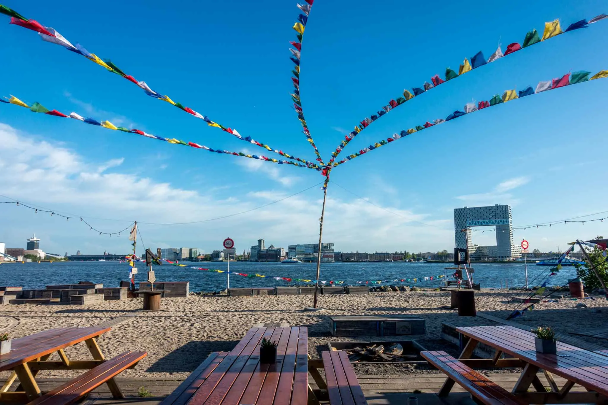 Picnic tables on a beach with flags flying overhead.