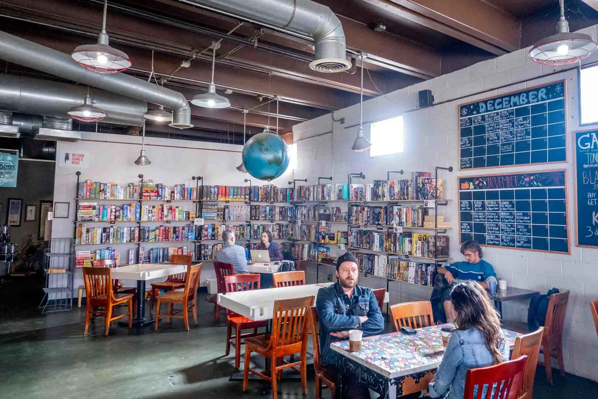 People sitting at cafe tables in front of a wall full of board games