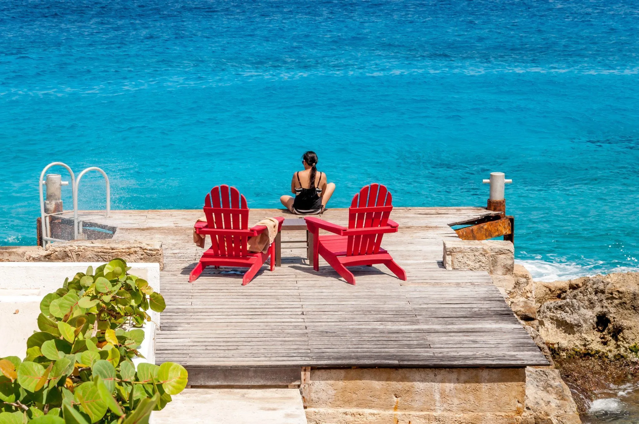 Woman sitting on a small dock with red beach chairs