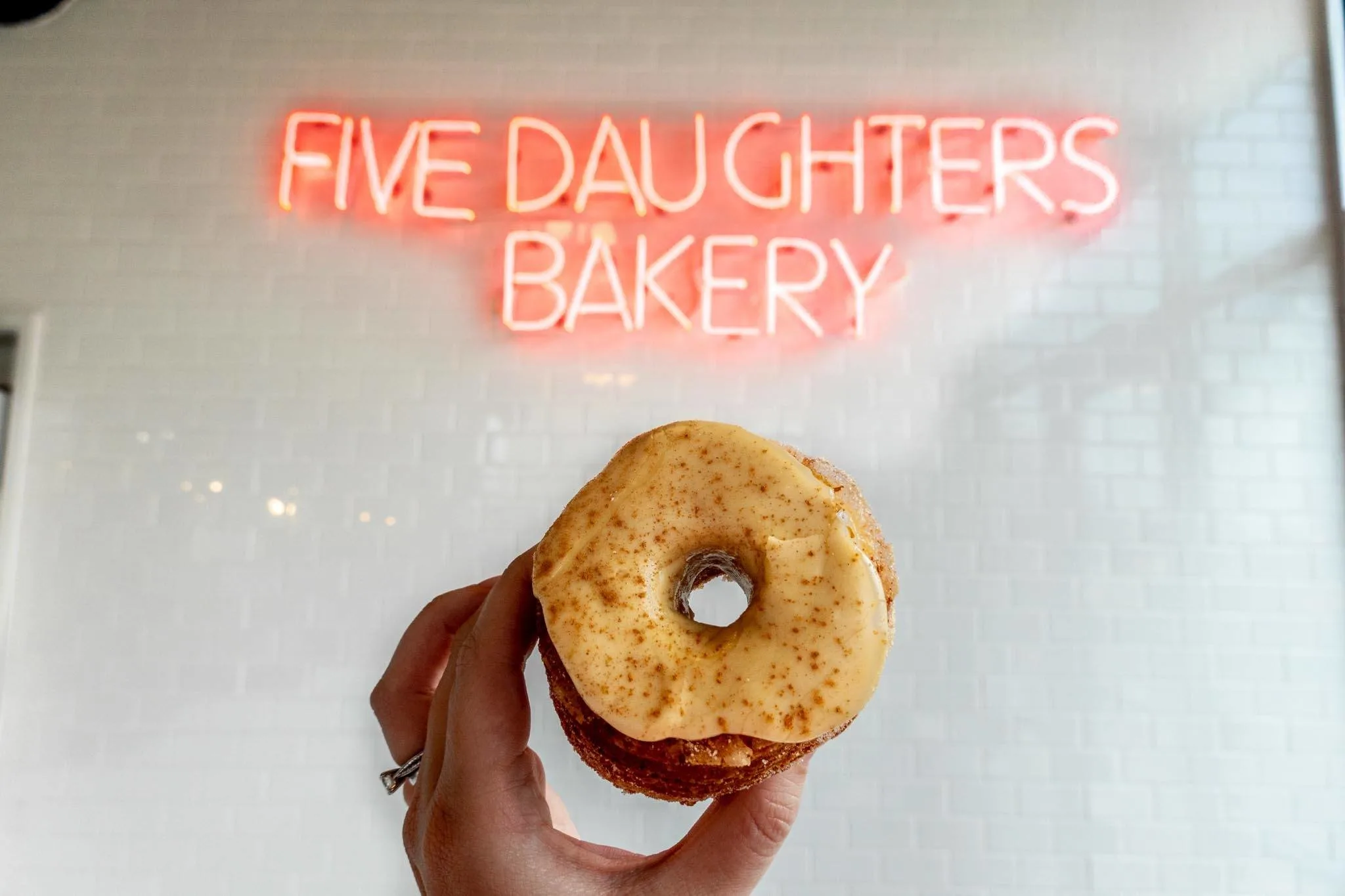 Maple glazed donut under the illuminated Five Daughters Bakery sign