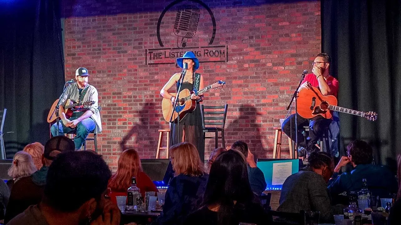 Three guitar players seated on stage. 