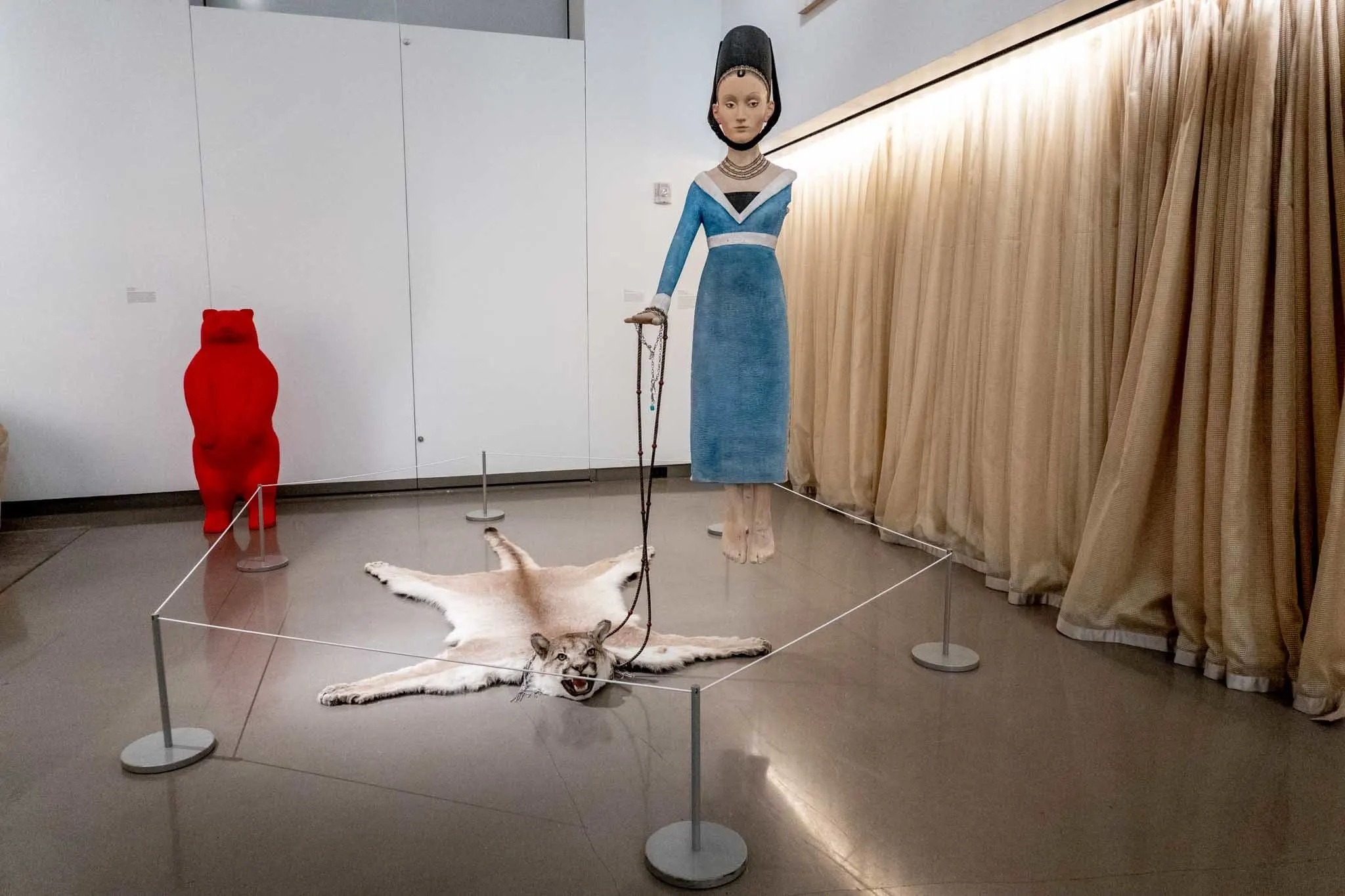 Art exhibit of a woman holding a leash attached to a puma skin rug