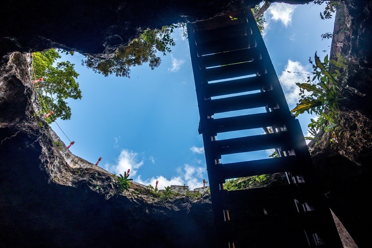 Looking up at the sky from inside a closed cenote under a staircase