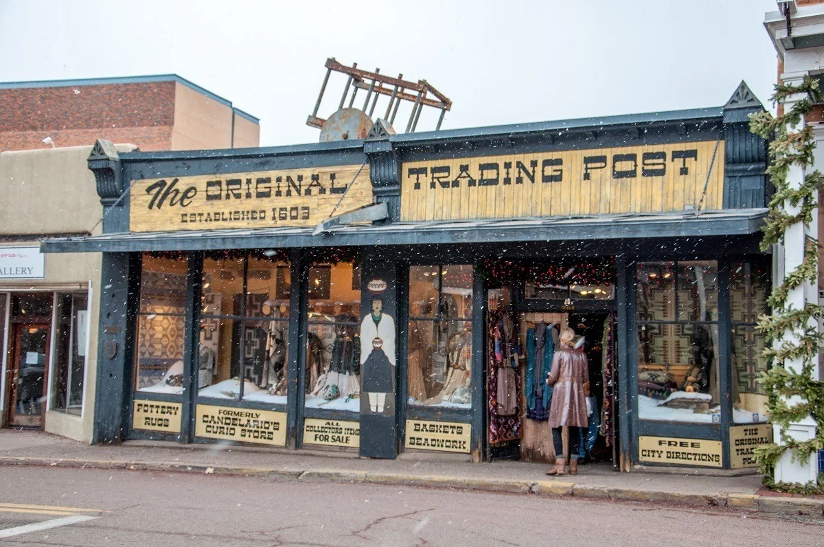 Woman entering a store with signage for "The Original Trading Post, established 1603"