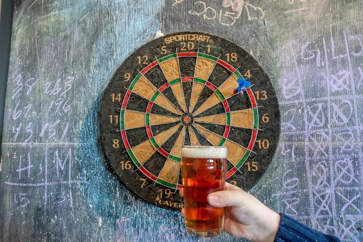 Hand holding a beer glass in front of a  dartboard.