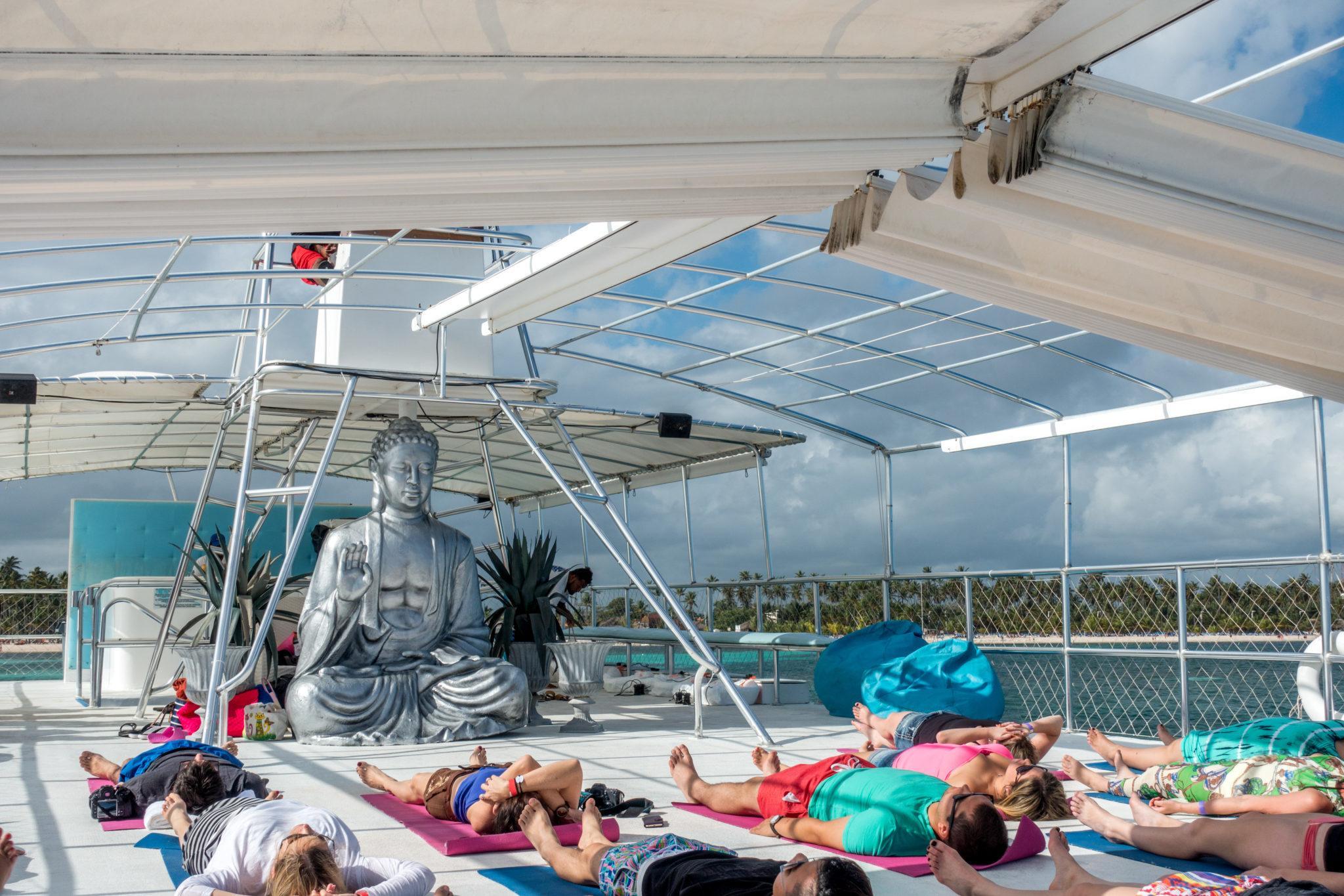 People doing yoga on a boat in front of Buddha statue