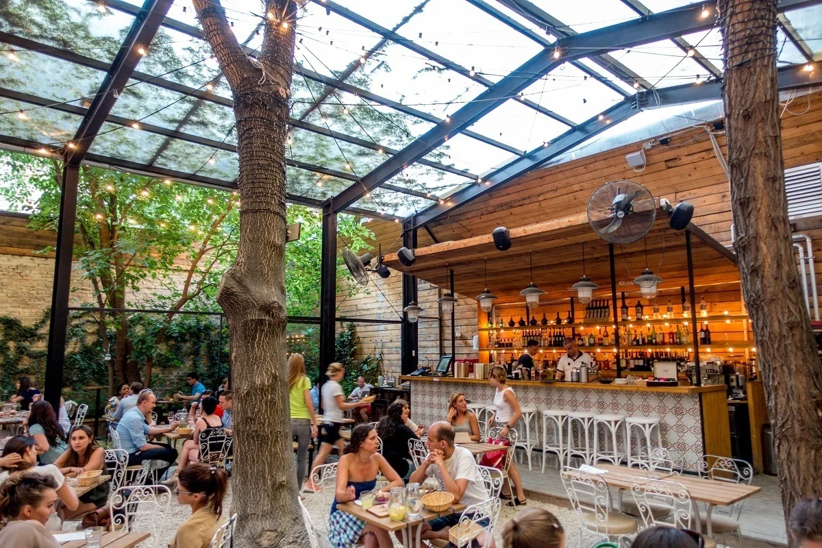 People eating at tables under trees beside a well-stocked bar
