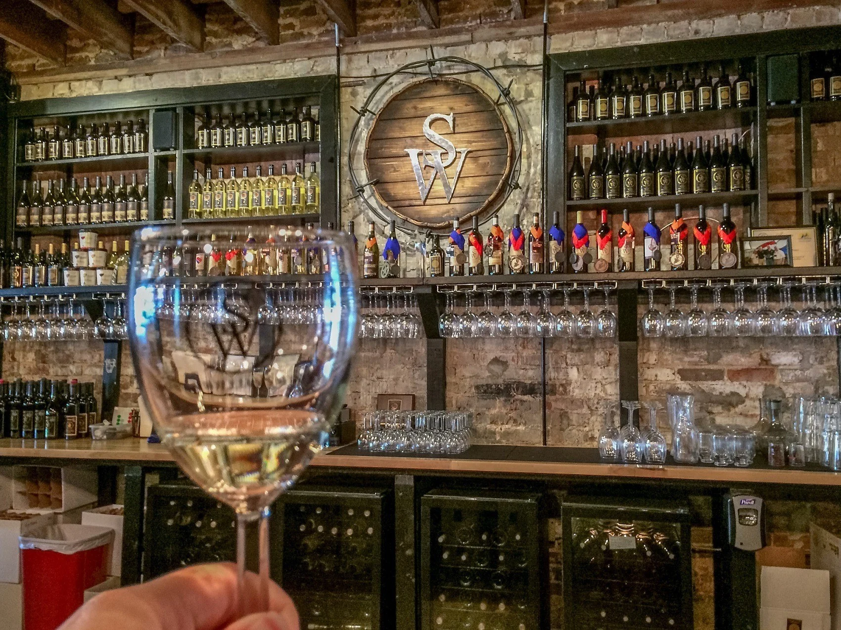 Wine glass in front of a bar with glasses and wine bottles.