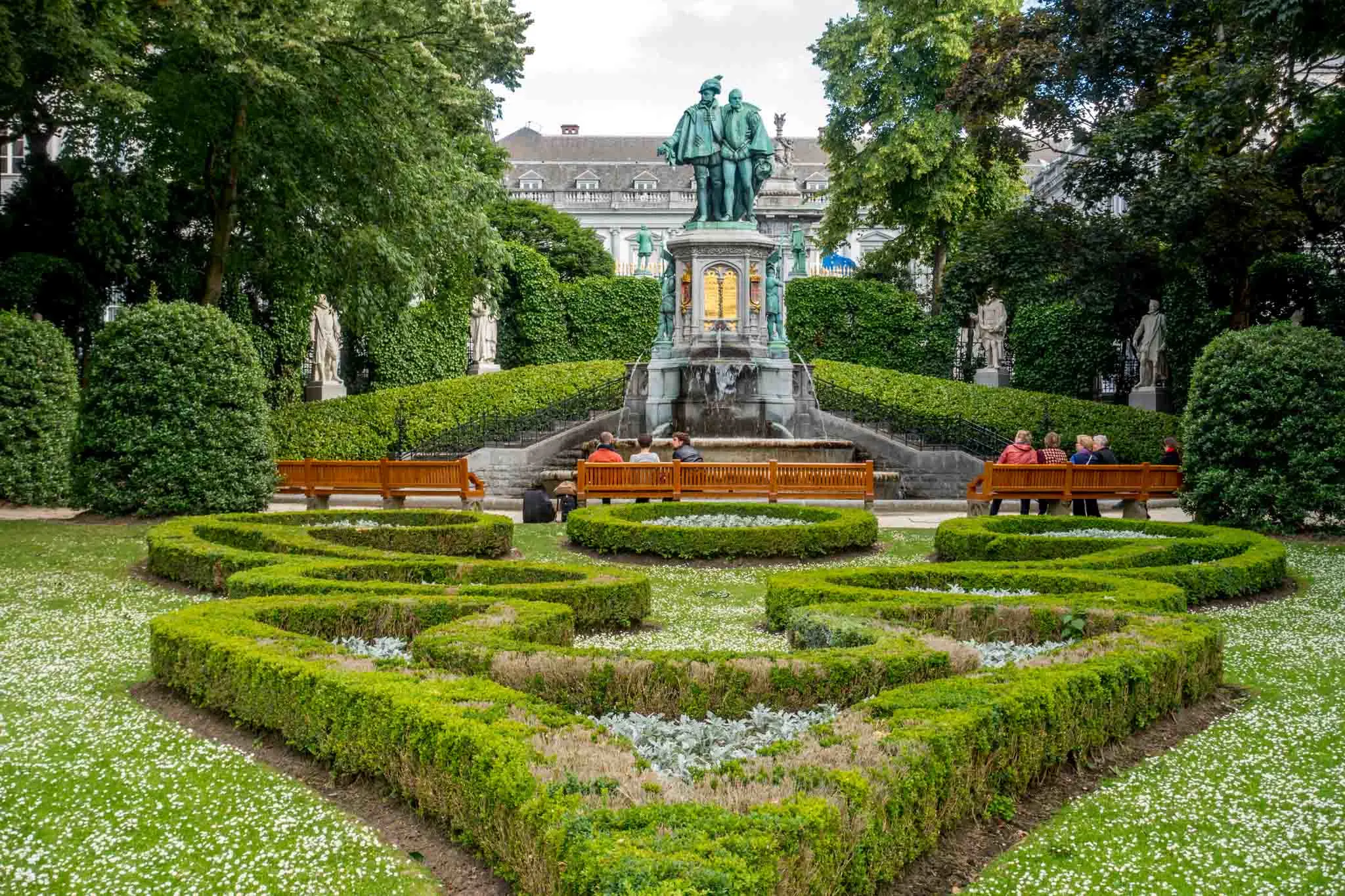 Park with manicured garden, fountain, and visitors on benches.