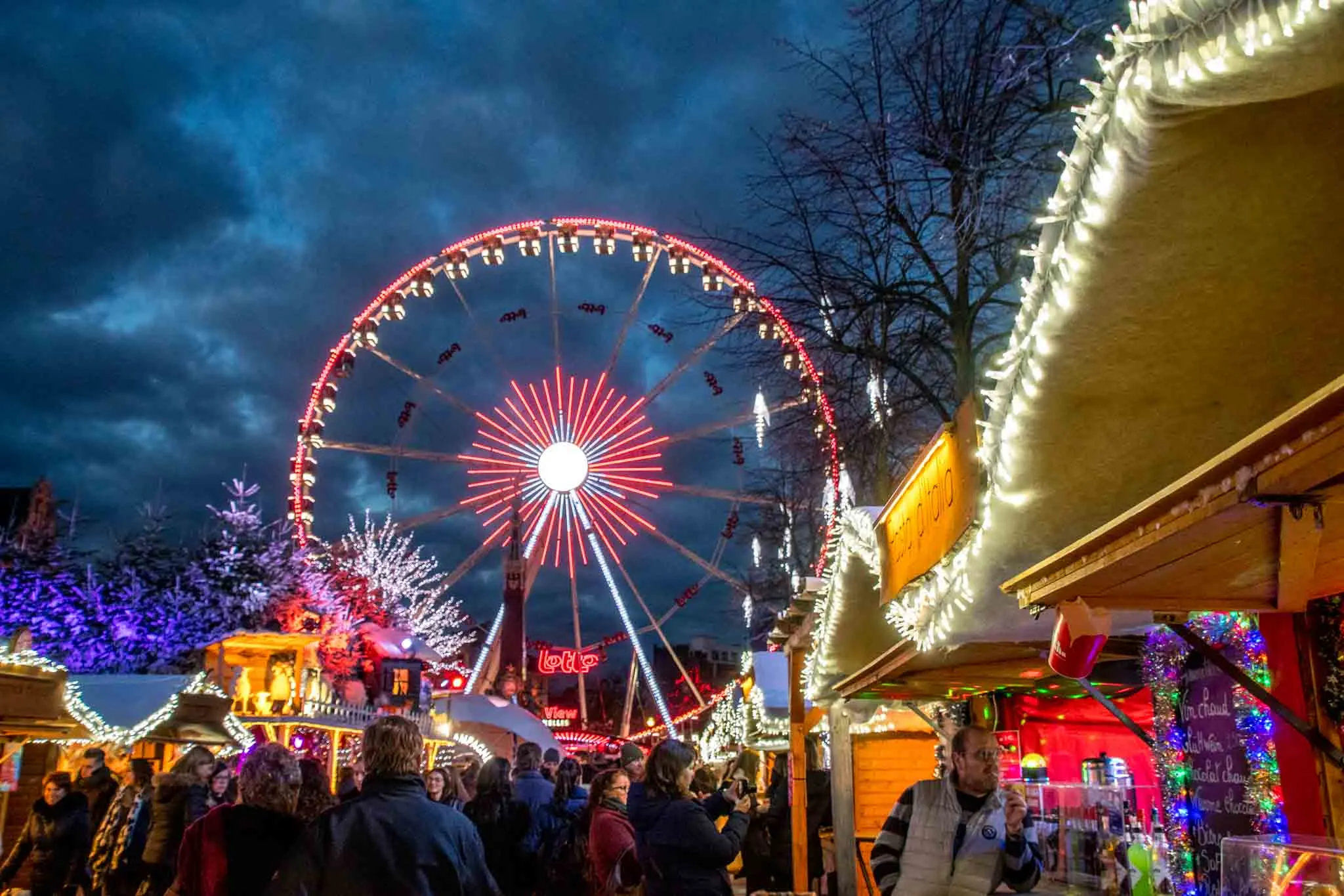 Ferris wheel, vendors, and shoppers at Christmas market.
