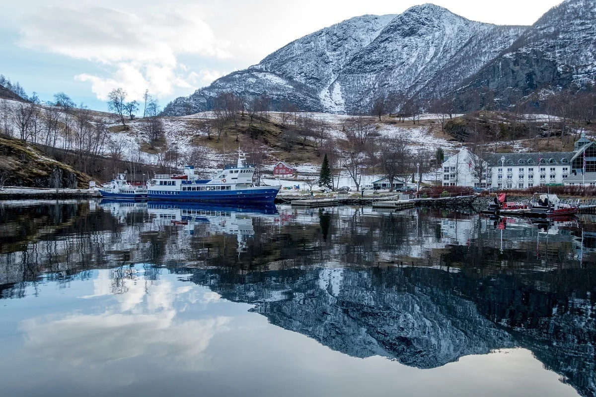 A boat in the harbor in Flam with a reflection of a mountain in the water.