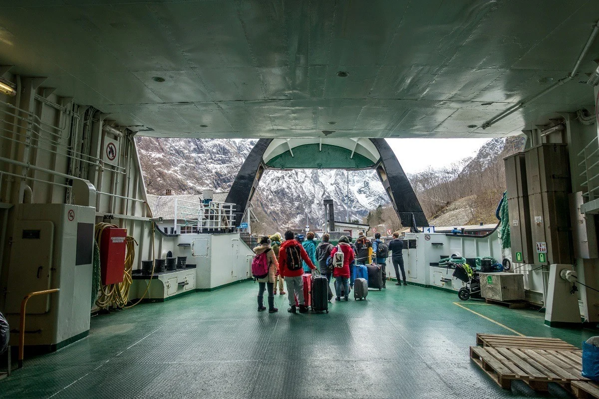 People disembarking a ferry with a snow-covered mountain in front of them.