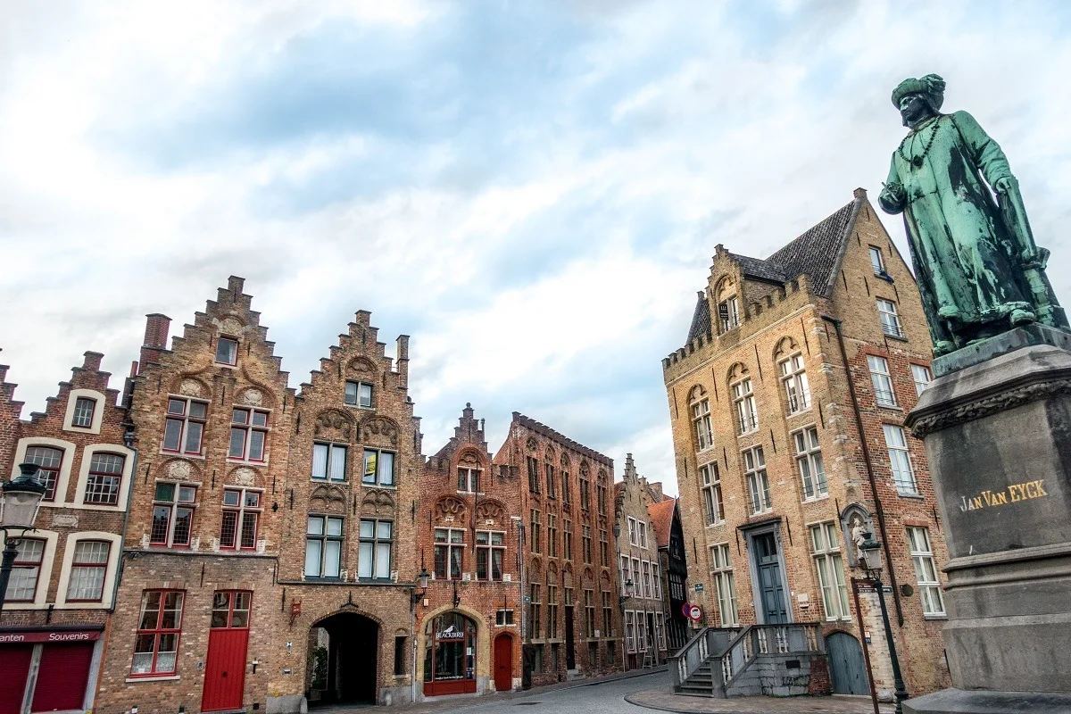Statue of Jan Van Eyck beside medieval merchant houses.