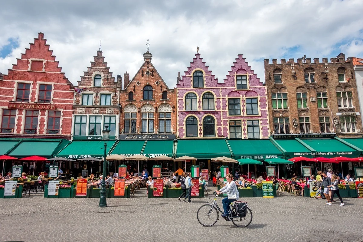 Woman bicycling by restaurants built in old guild houses 