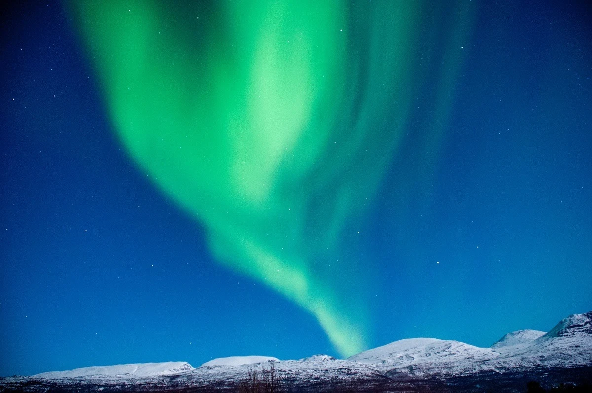 Green Northern Lights display over snowy hills