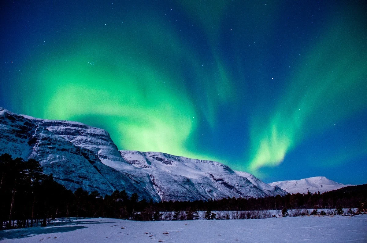 The green Northern Lights near Tromso over the snow-covered mountains