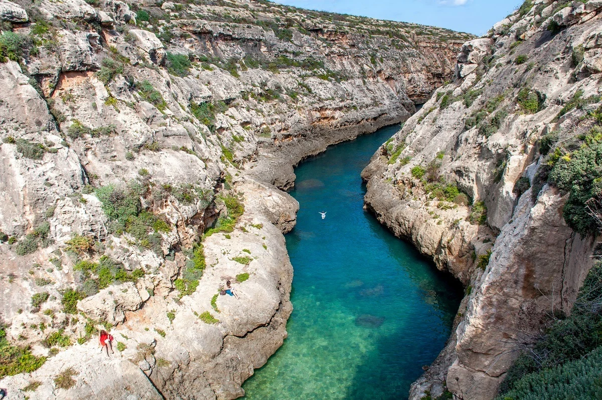 Person swimming in ocean inlet between cliffs