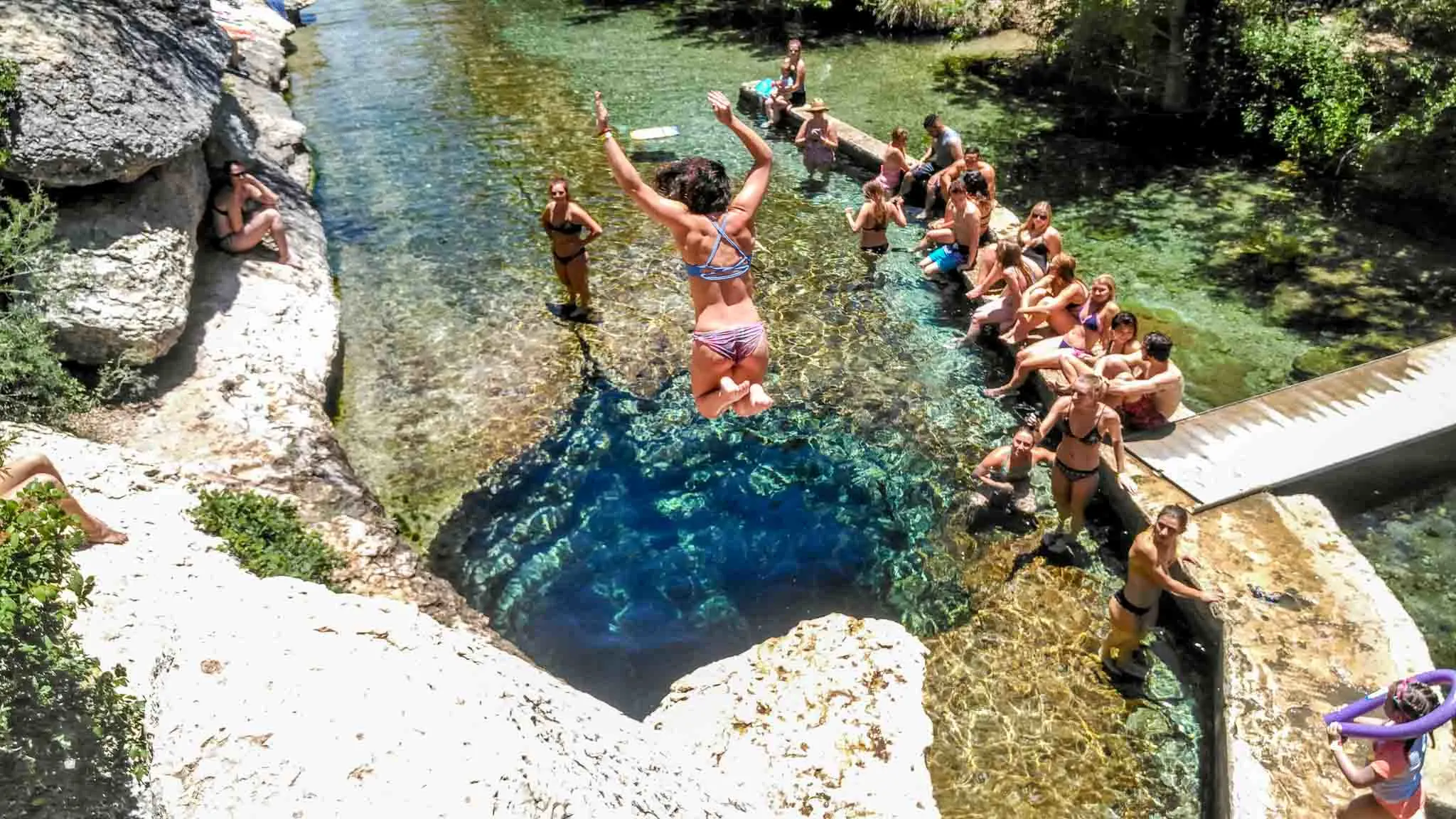 Woman jumping into into deep water with onlookers nearby.