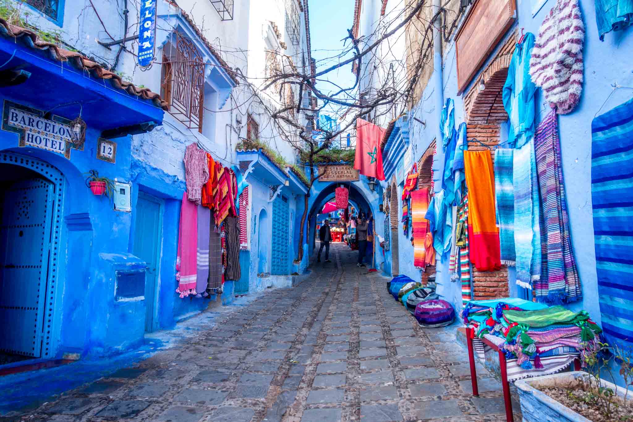 Bright rugs hanging on blue walls along a pedestrian walkway.