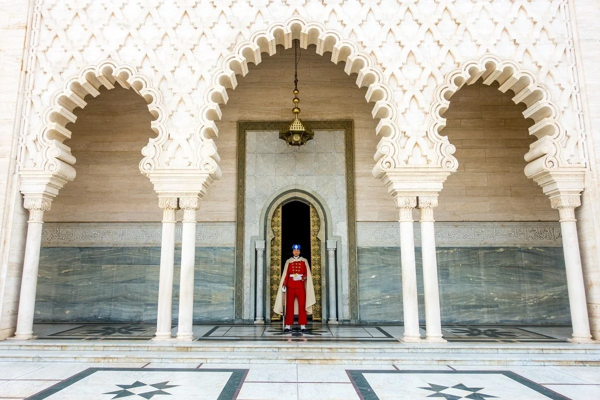 Man in a red uniform standing underneath white arches.