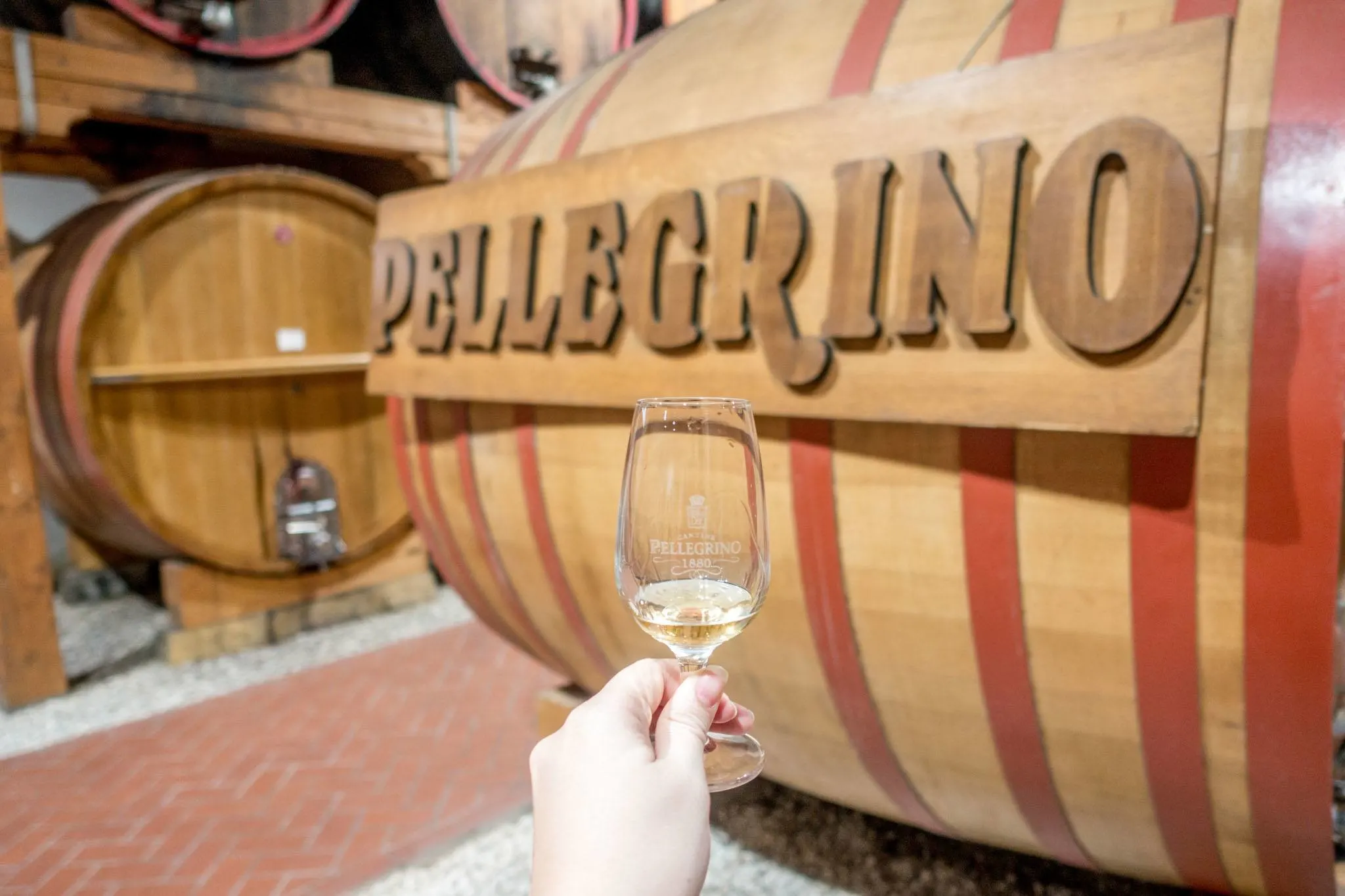 Glass of Marsala wine in front of a wine barrel labeled "Pellegrino"