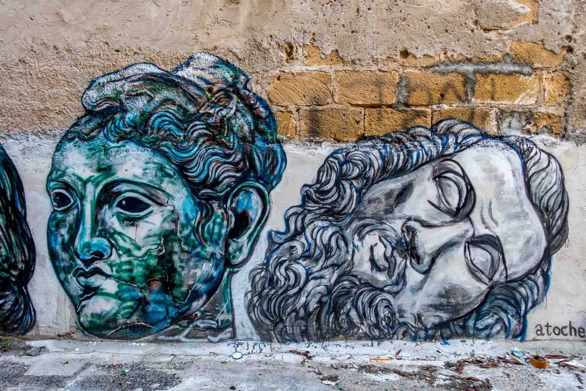 Two heads in a street art mural signed by artist Atoche.