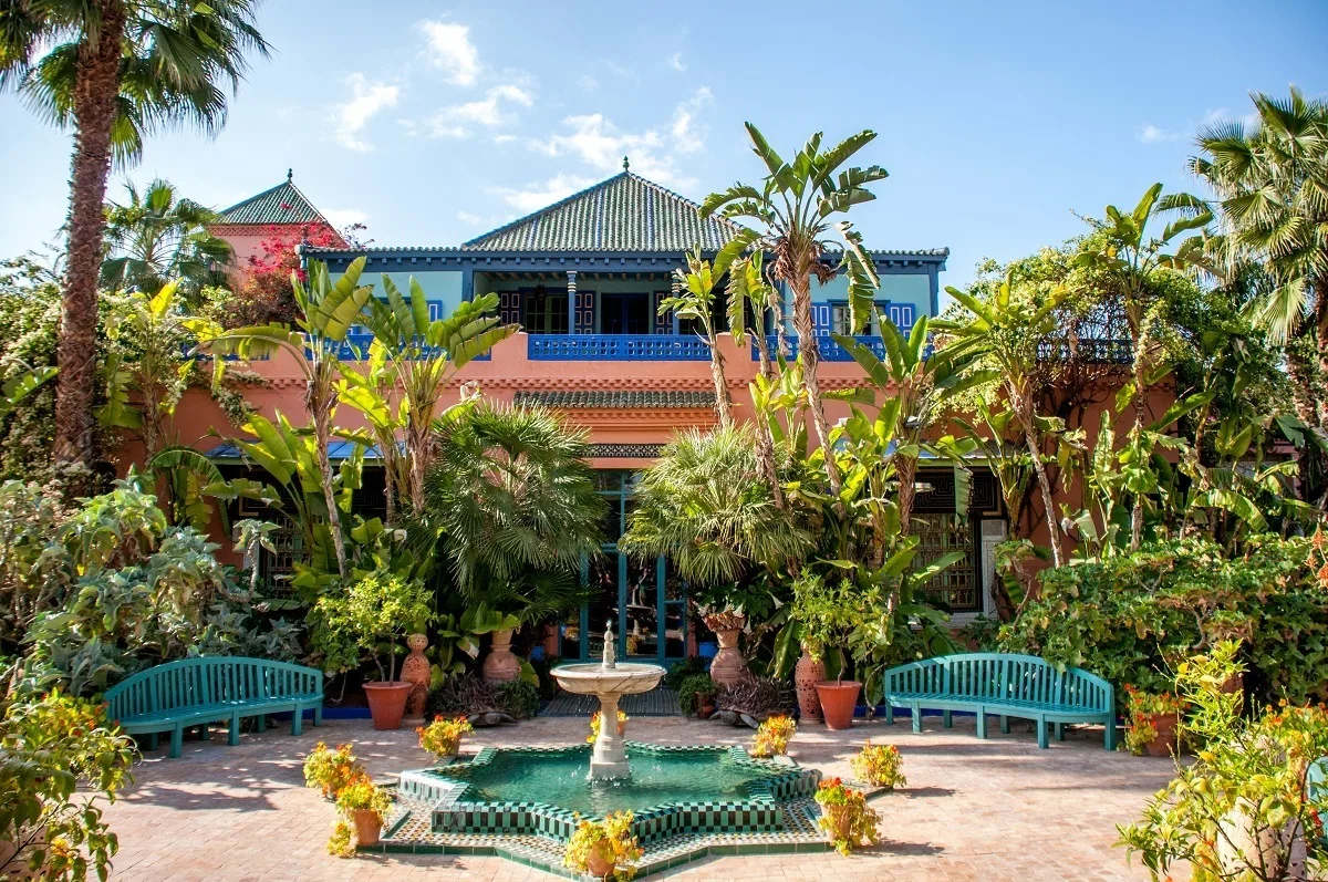 Pink and blue building behind lots of plants and trees.