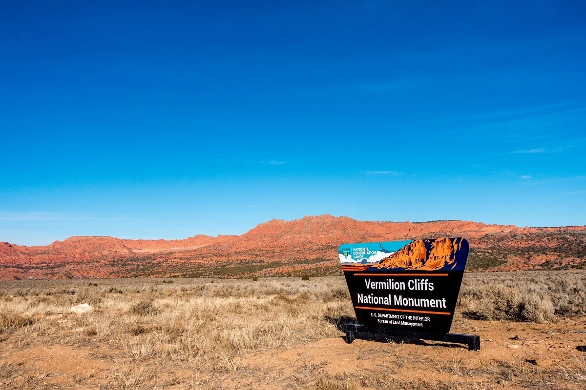 Sign for the Vermilion Cliffs National Monument in front of red hills