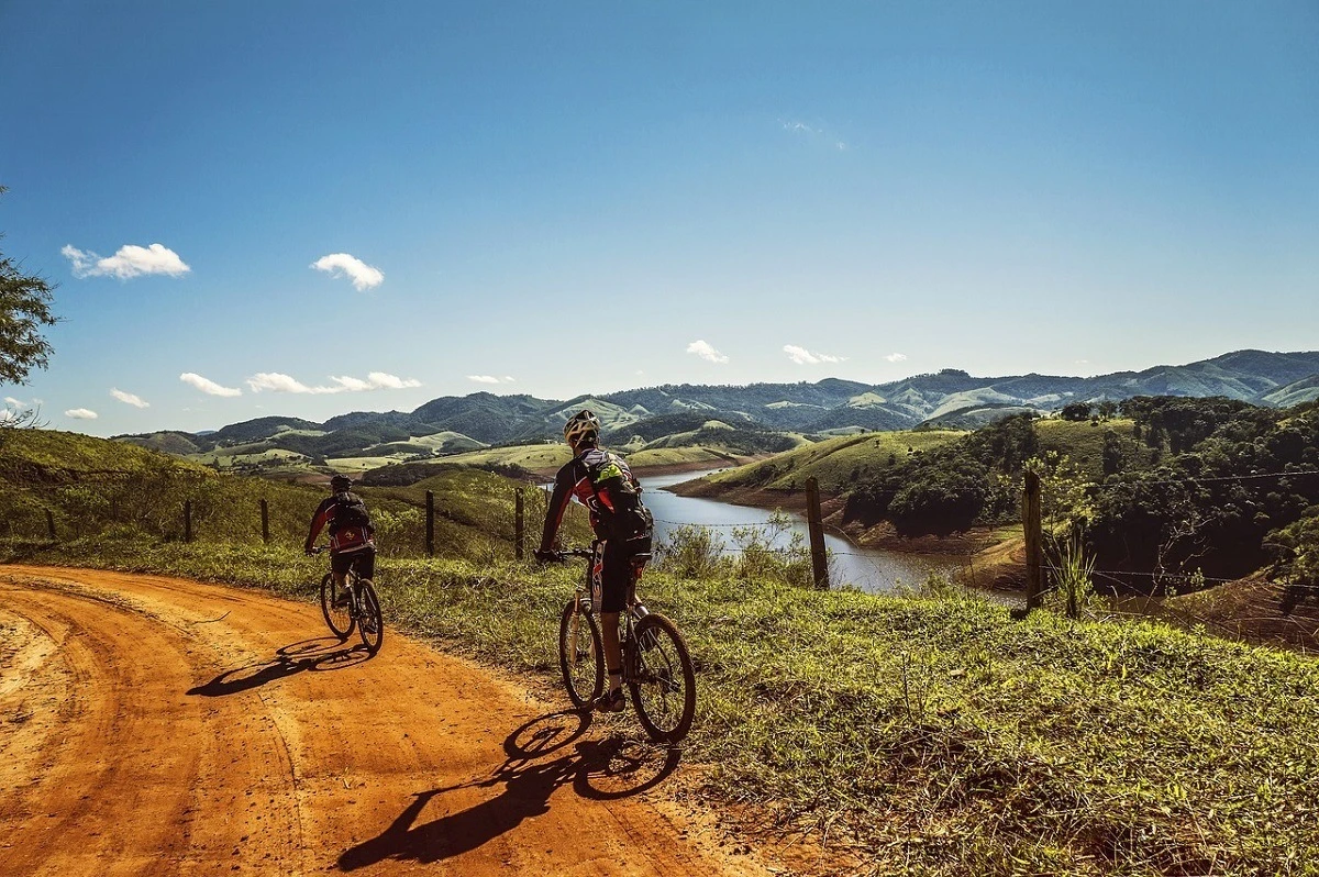 People mountain biking along a dirt road above a river in the rolling hills