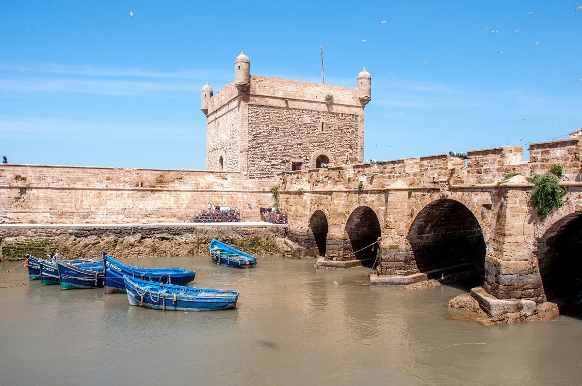 Blue fishing boats beside a stone bridge and city wall.