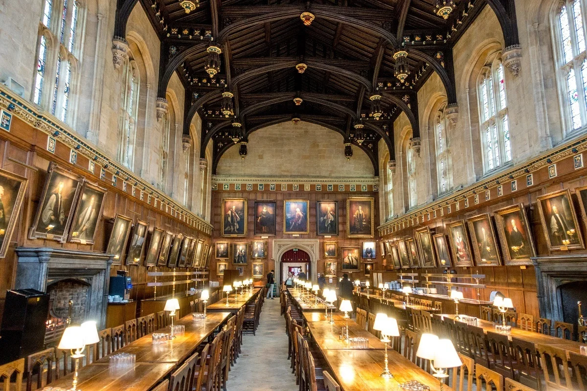 A dining hall with long tables and portraits along the walls.