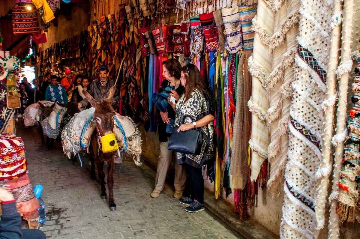 Donkey carrying goods through a market as people look on.