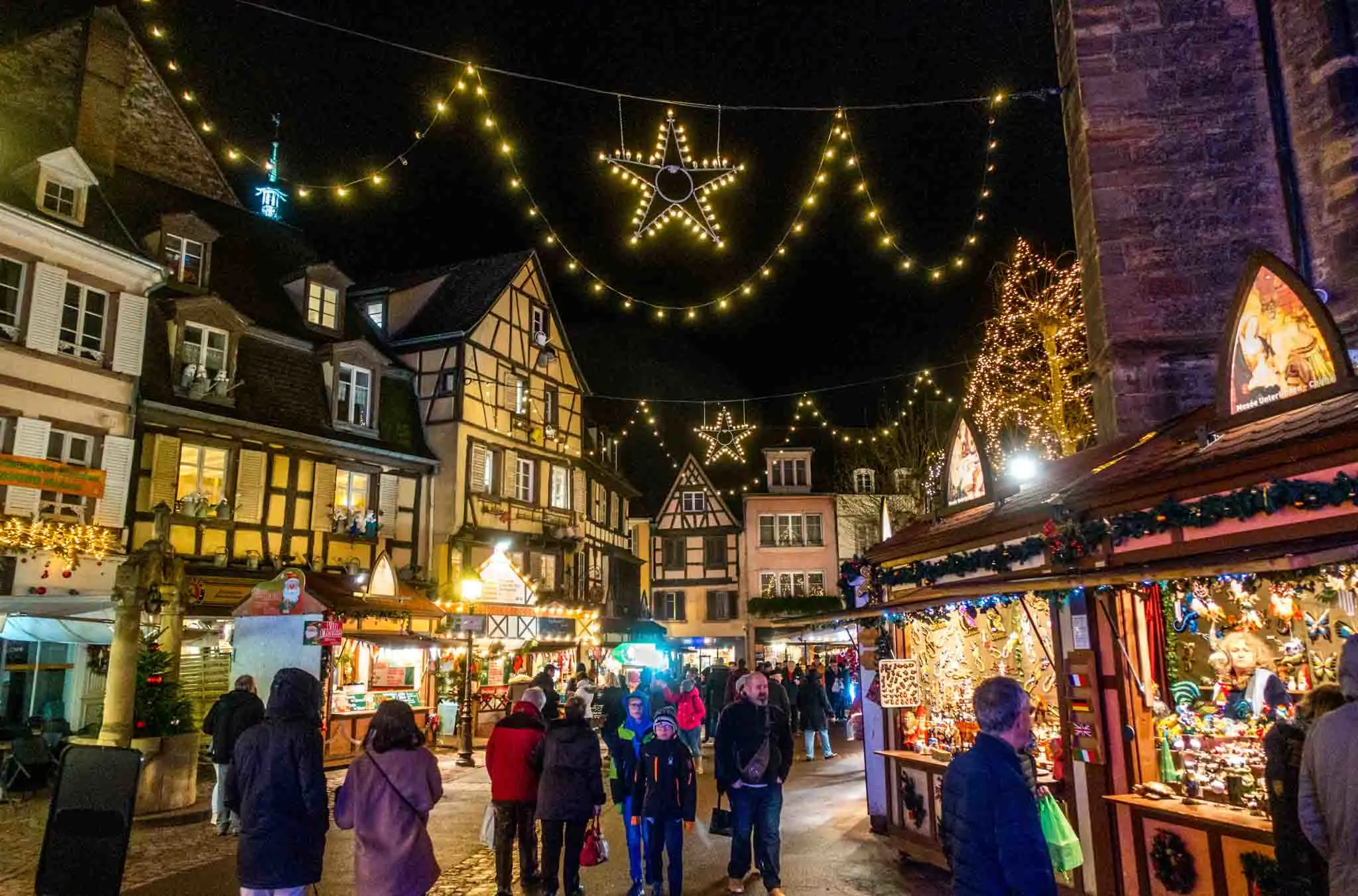 People shopping at market stalls under Christmas lights at night