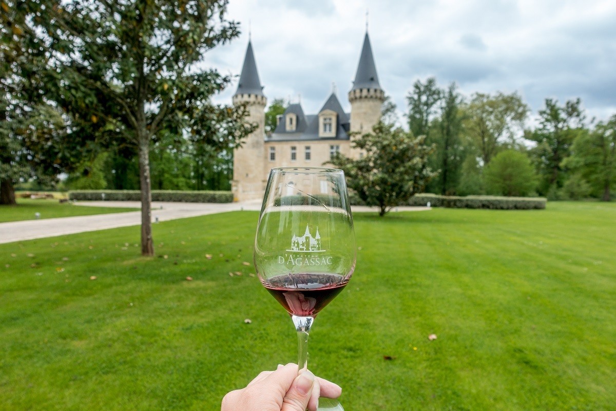 Wine glass held up in front of the exterior of a castle-like building, Chateau d'Agassac. 
