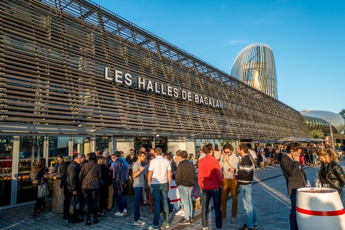 People enjoying happy hour outside a food hall with a gin for "Les Halles de Bacalan." 